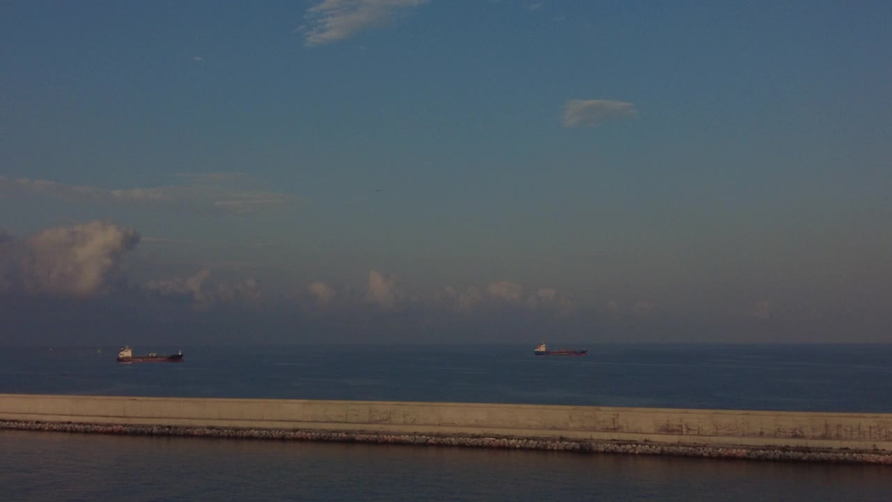 巴塞罗那港口的防波堤，背景是商船，天空中有一架飞机视频素材