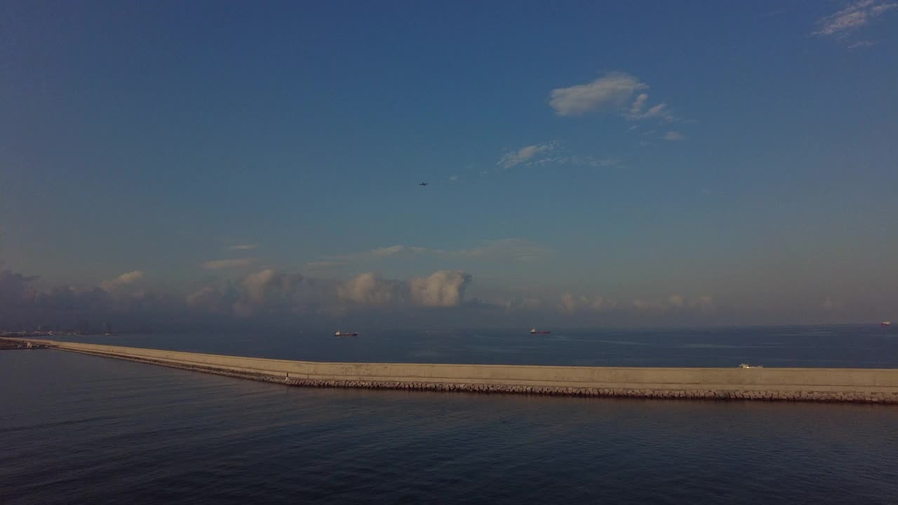 巴塞罗那港口的防波堤，背景是商船，天空中有一架飞机视频素材