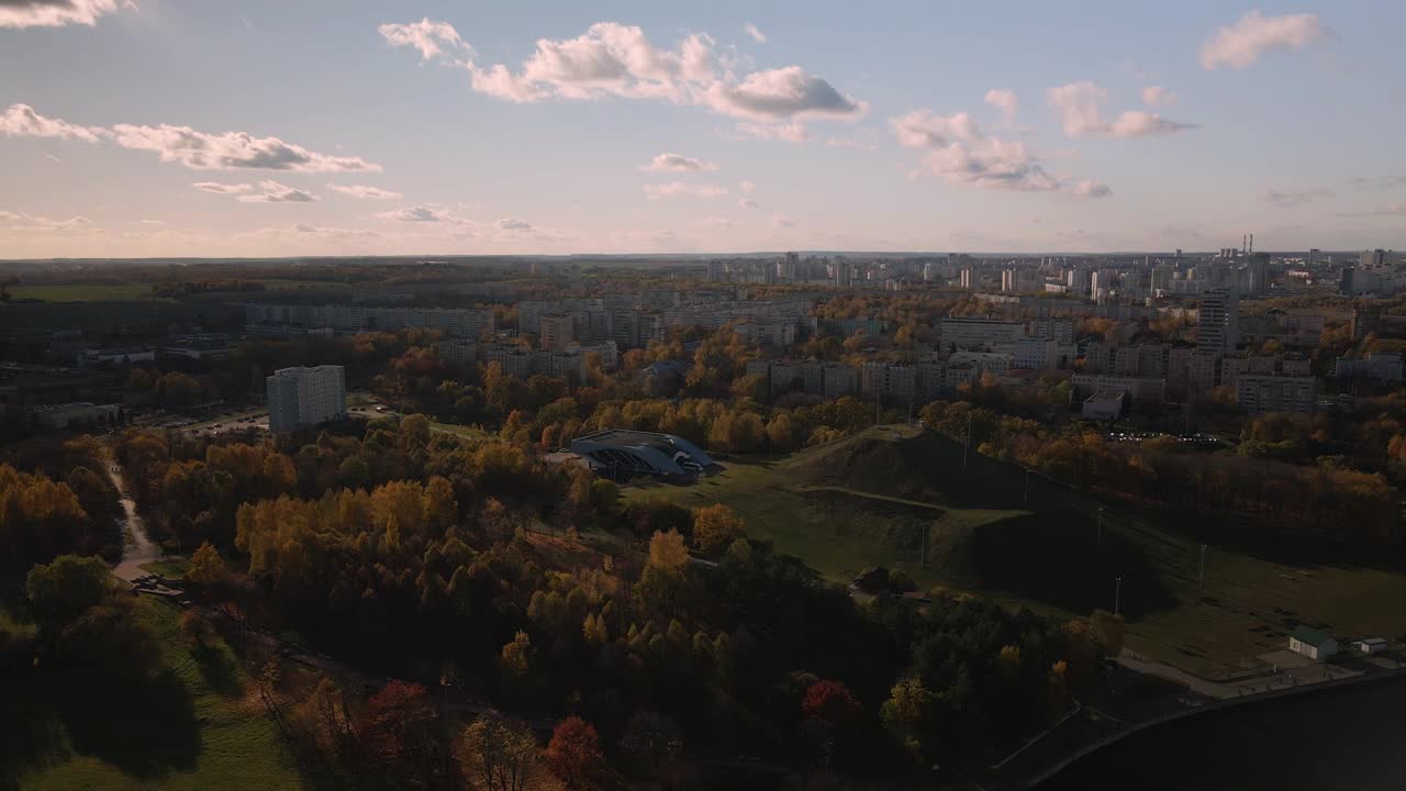 飞越秋天的公园。秋叶黄黄的树木随处可见。在地平线上有蓝色的天空和城市的房屋。公园的湖面清晰可见。航空摄影。视频素材