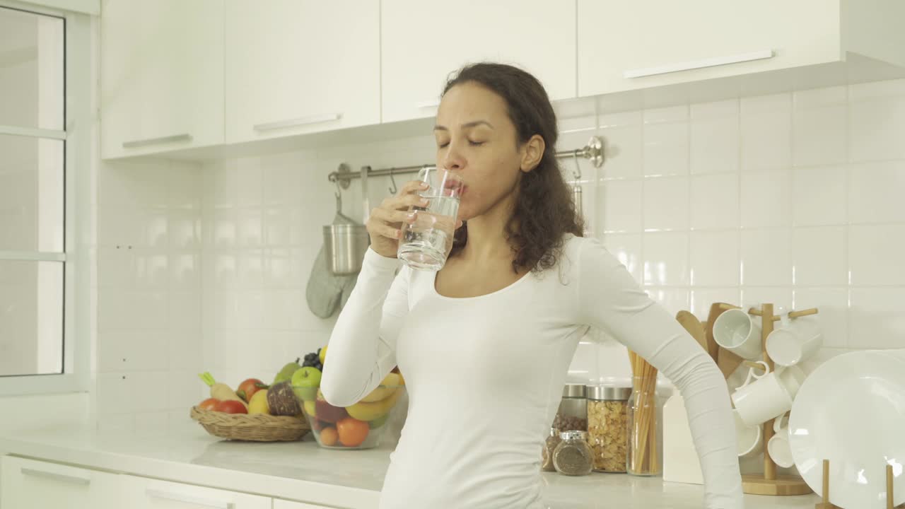 快乐的拉丁妇女在家里的厨房里喝一杯水的肖像。人们的生活方式。新鲜。视频素材