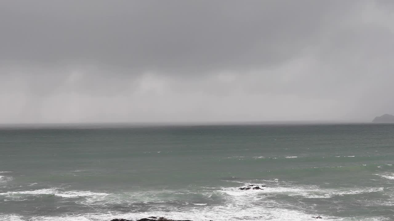 海上地平线上的雨云，与海浪拍打着海岸线上的岩石，有着复制的空间视频素材