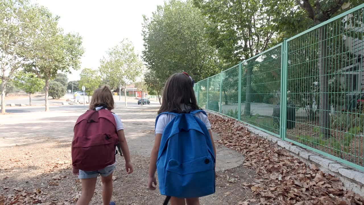 一个黑发的女孩和另一个金发的女孩背着书包，走在去学校的路上。教育和返校观念。视频素材