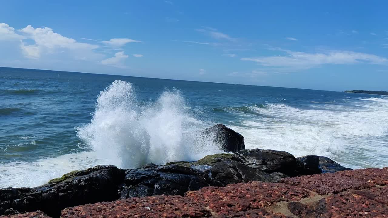 在阳光明媚的日子里，蔚蓝的天空下，白色的海浪拍打着海边的岩石视频素材