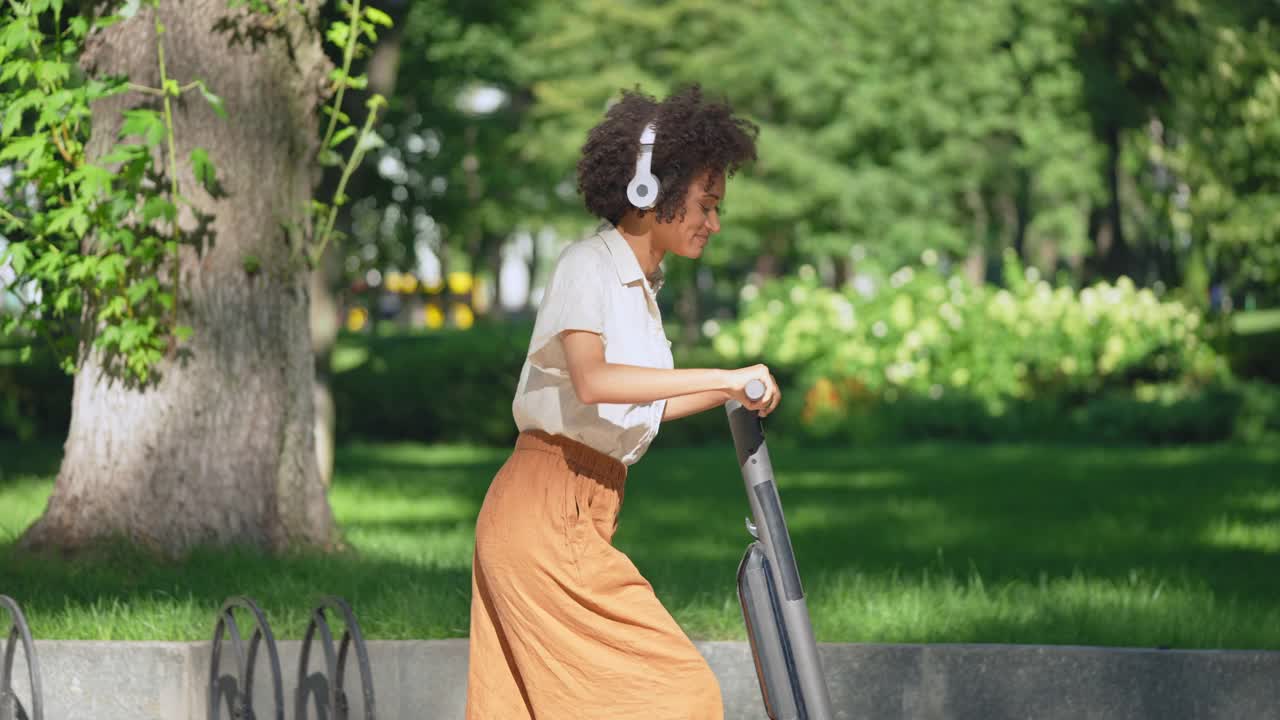 快乐的女人戴着耳机骑着电动车在城市公园，享受她的一天视频素材