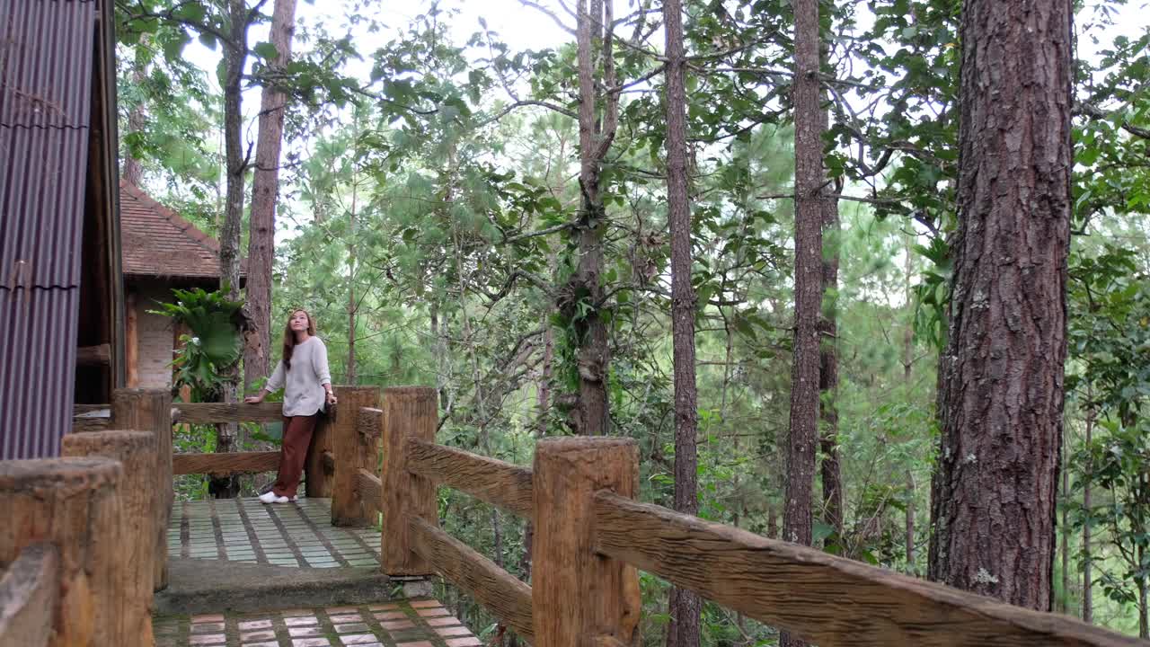 一个年轻的女人站在树林里的小木屋前视频素材