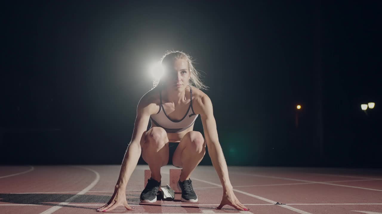 在体育场的黑暗中，一位妇女正准备在跑道上开始一场比赛。慢镜头女子从体育场黑暗中的绝食开始视频素材