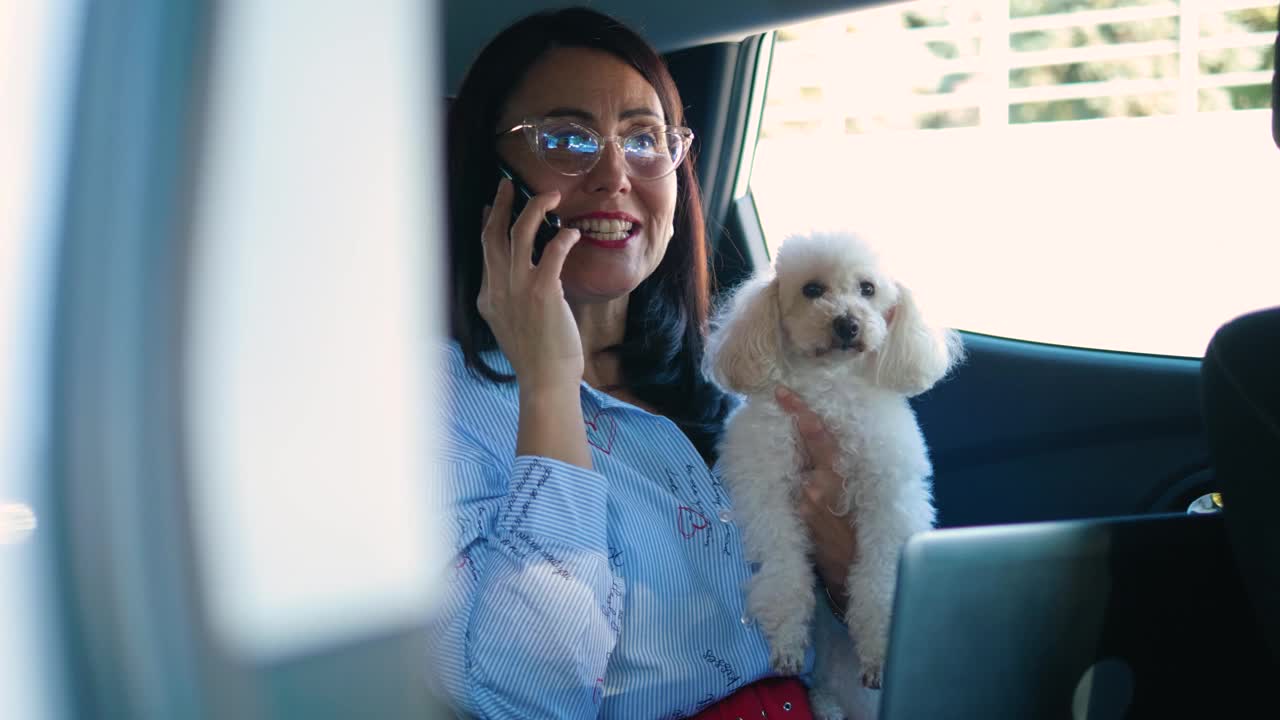 一个微笑的女人坐在车后座上打电话，还抱着她的宠物视频素材