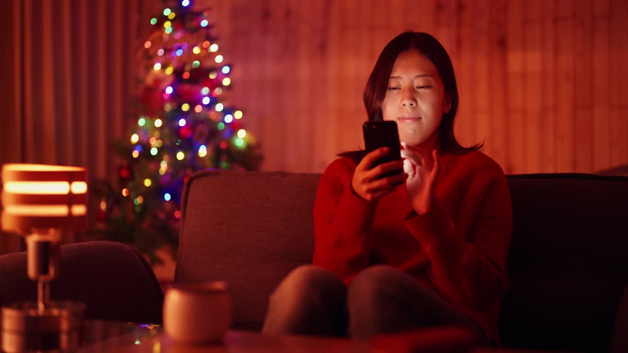 一名年轻女子在圣诞节晚上在家用智能手机网购视频素材