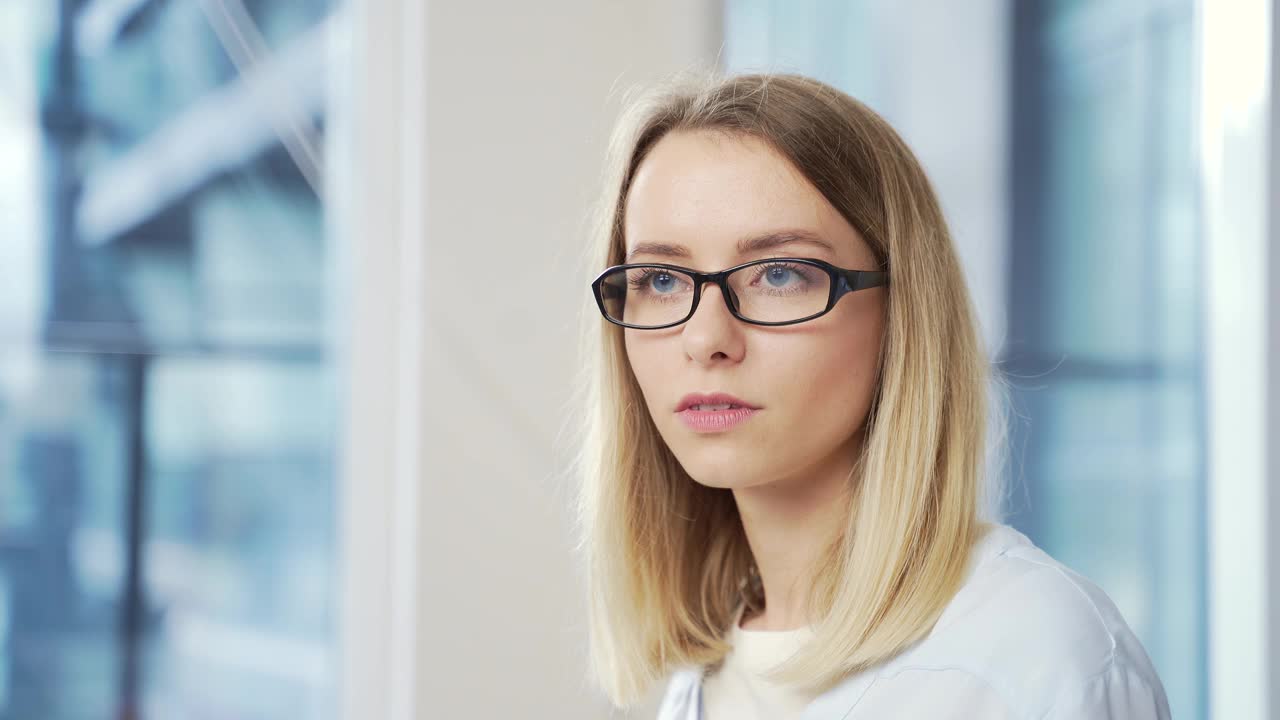 特写的一个年轻的成年金发商业妇女与眼镜看着相机视频素材