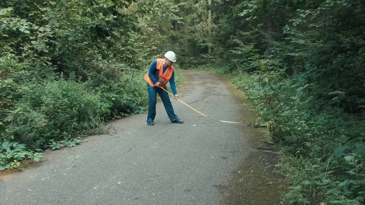 工人在工作服和在森林公路上用卷尺测量道路视频素材