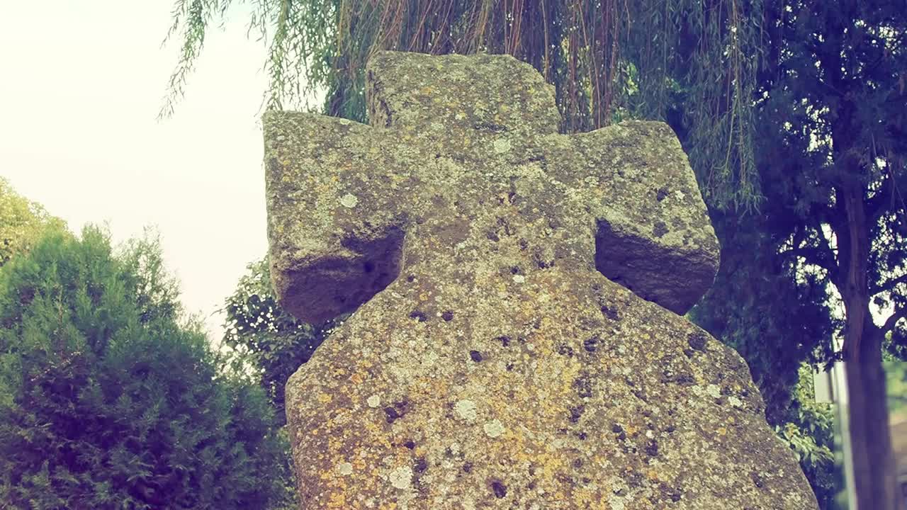 在夏天的白天，墓地里有一个古老的石头十字架。雾蒙蒙的模糊背景。万圣节的主题。长满青苔的十字架墓碑。诡异的神秘的地方。柳树摇曳。复古风格视频素材