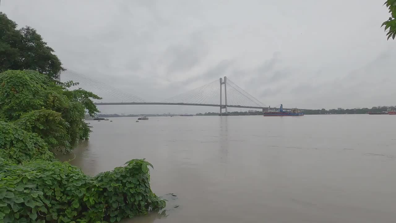 维德雅瑟格塞图(Vidyasagar Setu)或第二胡格利桥(Second Hooghly Bridge)，横跨胡格利河(Hooghly River)，在雨天的阴天里，前景中有框架树。印度西孟加拉邦的加尔各答视频素材