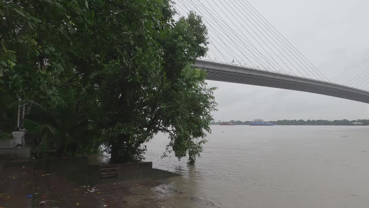 维德雅瑟格塞图(Vidyasagar Setu)或第二胡格利桥(Second Hooghly Bridge)，横跨胡格利河(Hooghly River)，在雨天的阴天里，前景中有框架树。印度西孟加拉邦的加尔各答视频素材