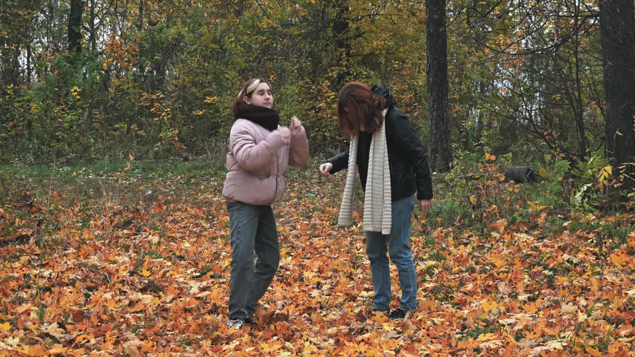 两个年轻的女孩在秋天黄色的公园里，在落叶上跳舞。视频素材