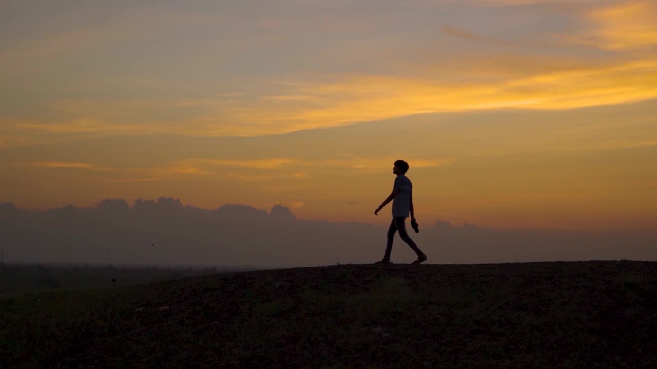 一个印度人的剪影，在蓝色的时间里，夕阳西下，走在橙色的云前。孤独的人走在橘色的云前。孤独的背景。视频素材