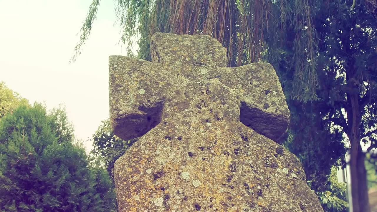 在夏天的白天，墓地里有一个古老的石头十字架。雾蒙蒙的模糊背景。万圣节的主题。长满青苔的十字架墓碑。诡异的神秘的地方。柳树摇曳。复古风格视频素材