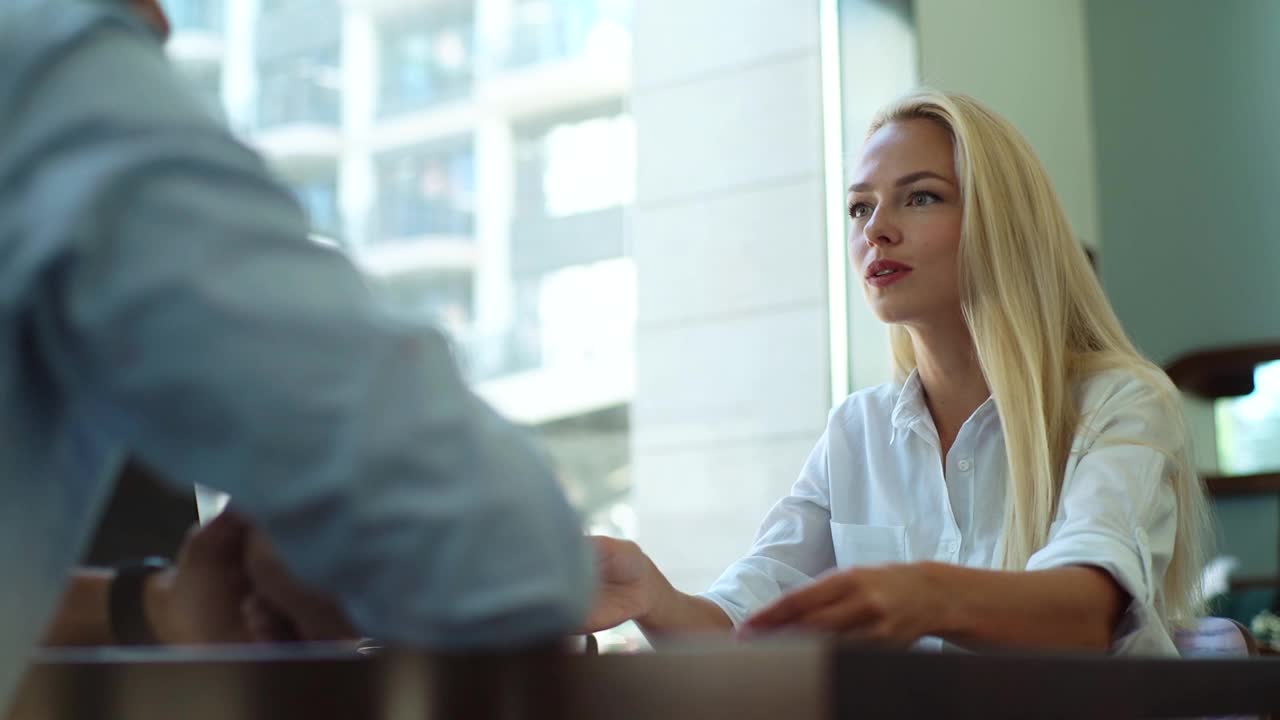 近距离低角度的迷人的年轻金发商业女人讨论项目与男同事在轻咖啡馆坐在桌子靠窗。视频素材