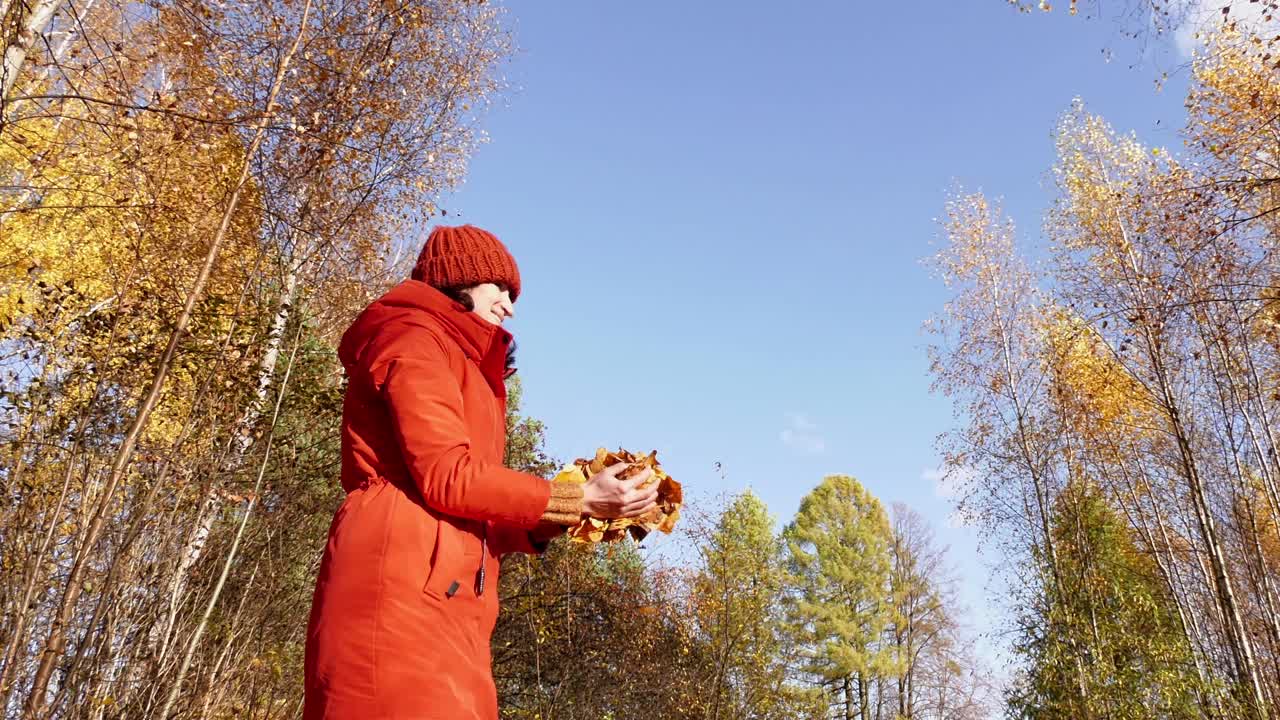 穿红夹克的女人扔黄叶。秋天的风景。慢动作视频视频素材