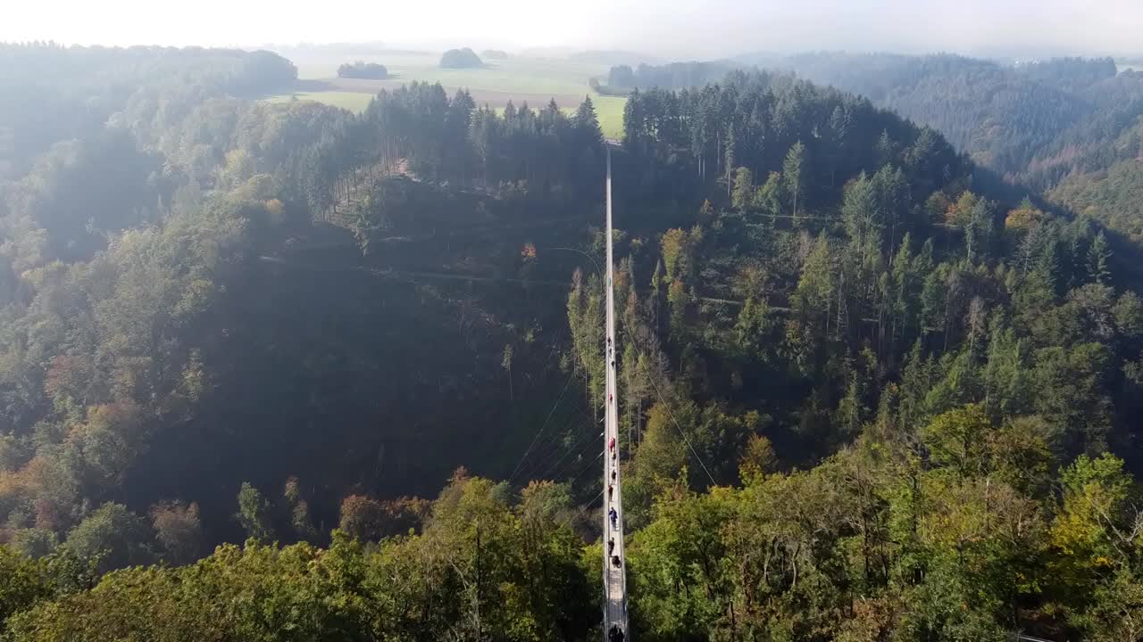 一架无人机飞过一座悬挂着钢索的木桥，俯瞰着西德一片茂密的森林，可以看到游客在桥上行走。视频素材