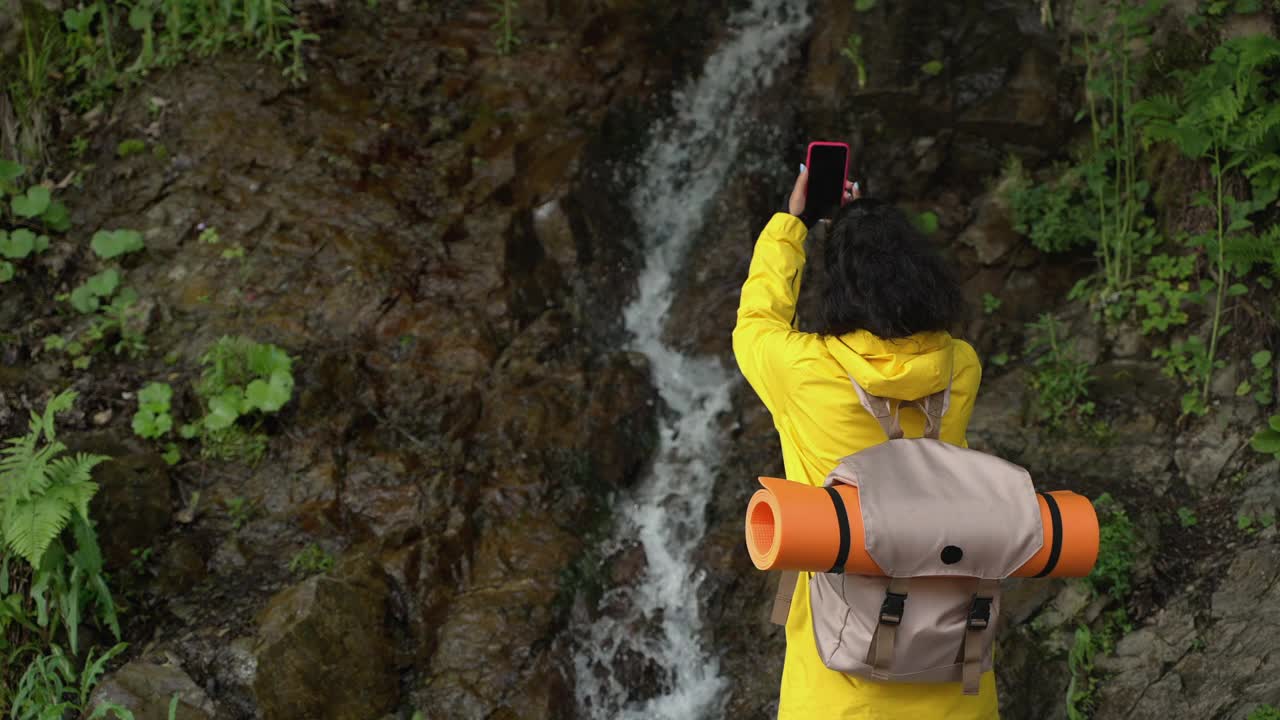 女孩徒步旅行者拍摄山上的瀑布视频素材