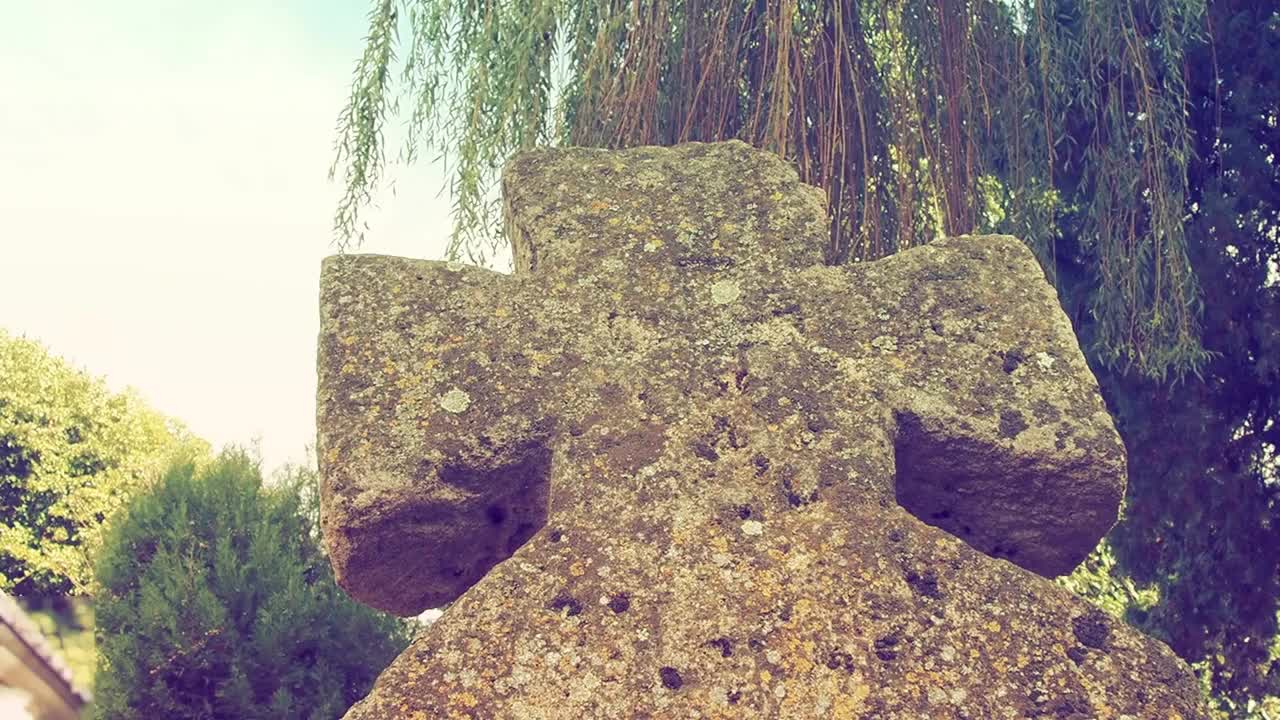 在夏天的白天，墓地里有一个古老的石头十字架。雾蒙蒙的模糊背景。万圣节的主题。长满青苔的十字架墓碑。诡异的神秘的地方。柳树摇曳。复古风格视频素材