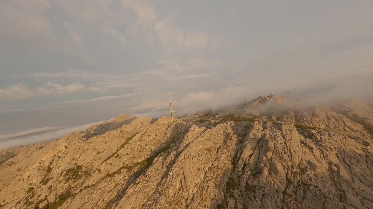 FPV视频，山地冲浪，在云中高速飞行与花岗岩山脉和天线农场在一个美丽的日出。坦皮奥包萨尼亚，撒丁岛，意大利。视频素材