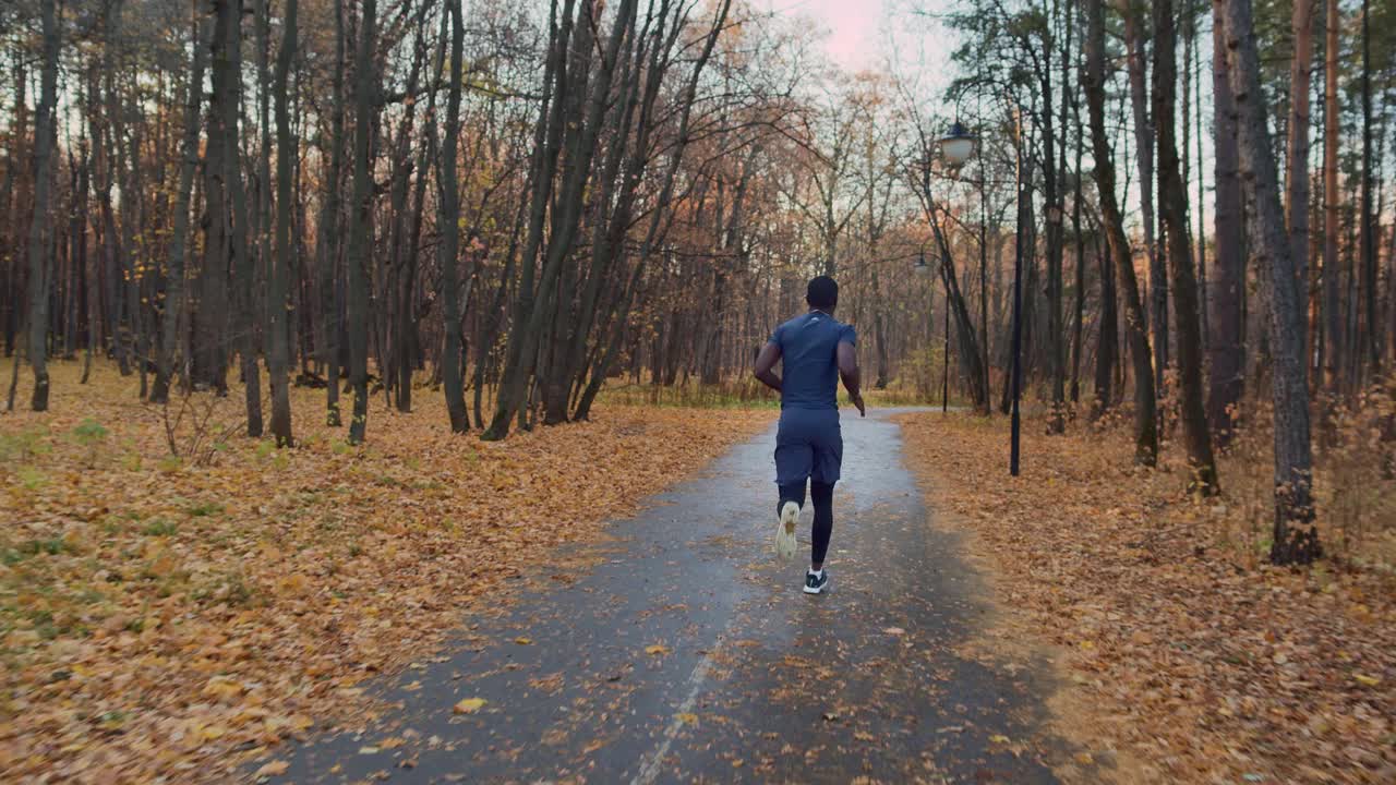 一个皮肤黝黑的男人雨后在一个旧公园里慢跑。良好的身体状态。为体育比赛的概念准备，后视镜。视频素材