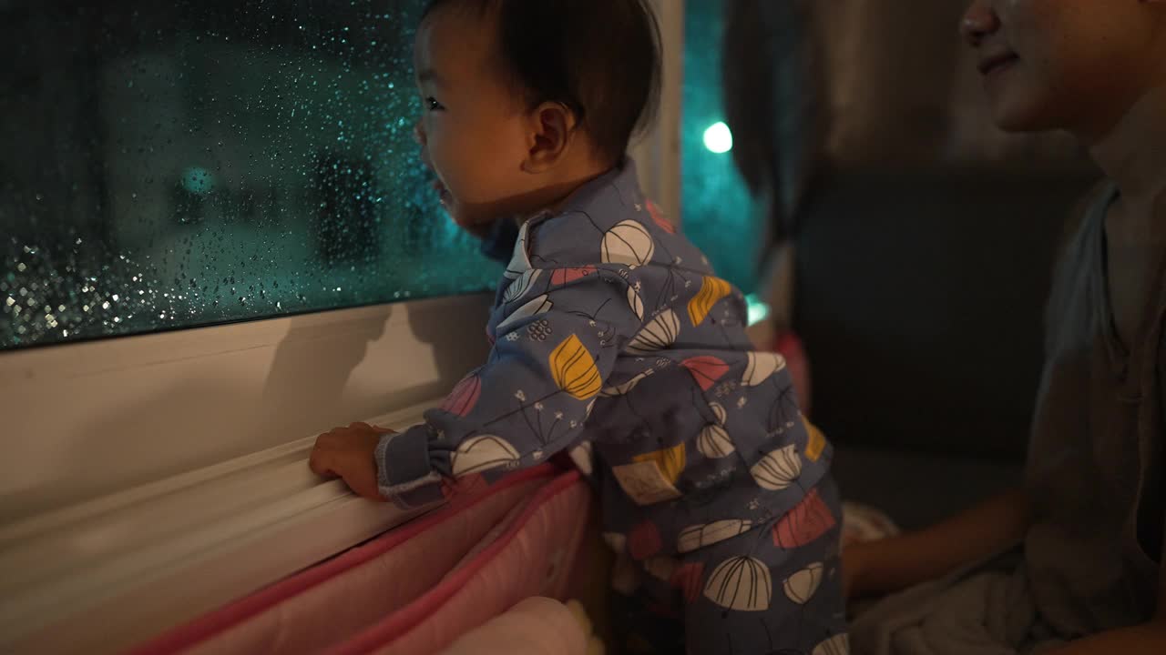 幸福时刻亚裔母女望着窗外下雨，等待父亲回家的家庭生活视频素材