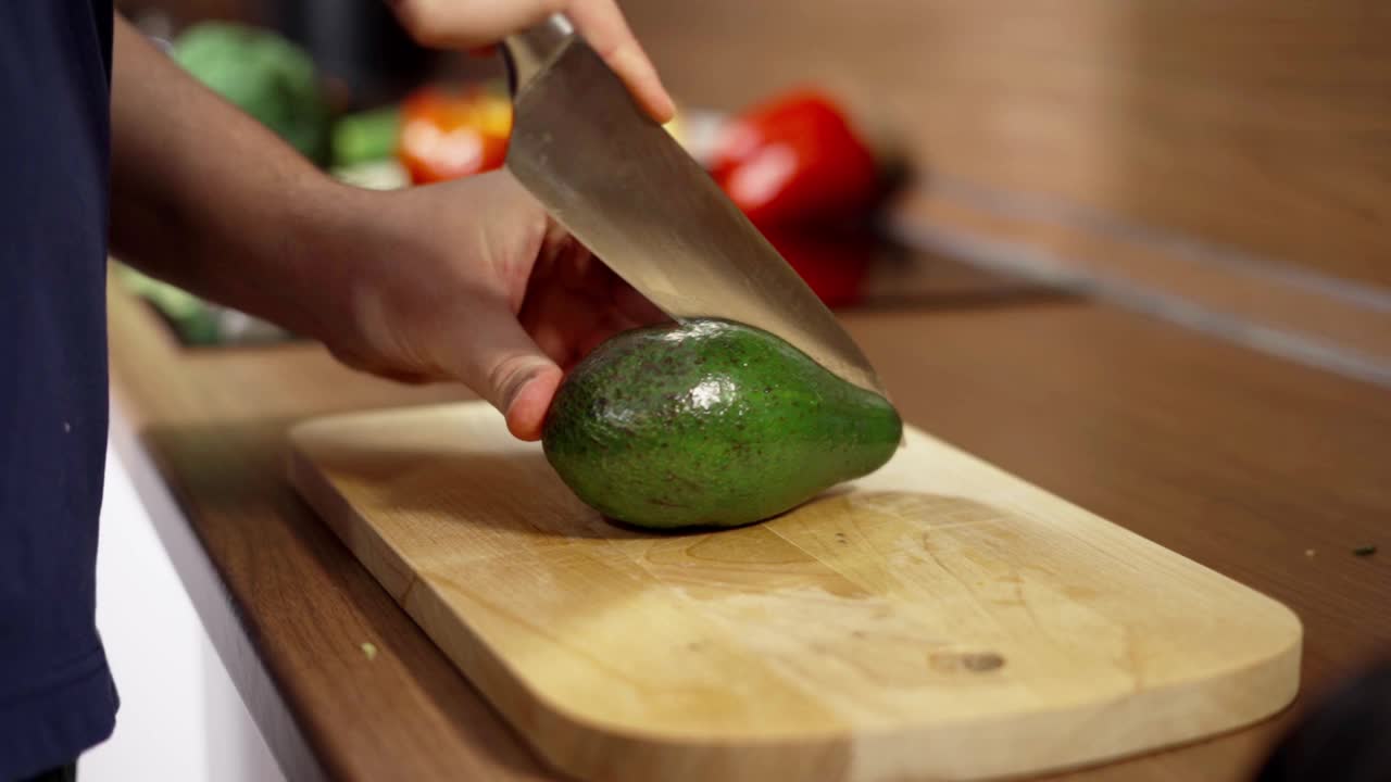 一个男人用菜刀在木制砧板上切一个新鲜的鳄梨。健康饮食。视频素材