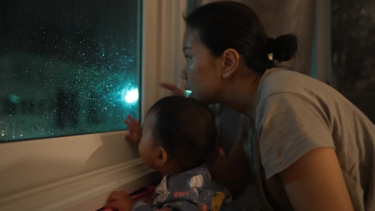 幸福时刻亚裔母女望着窗外下雨，等待父亲回家的家庭生活视频素材