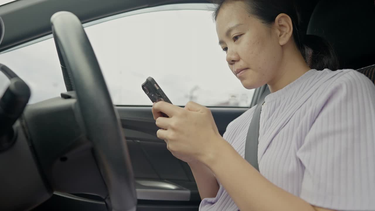 年轻的成年女性手握方向盘开车，另一只手在路上用手机视频素材