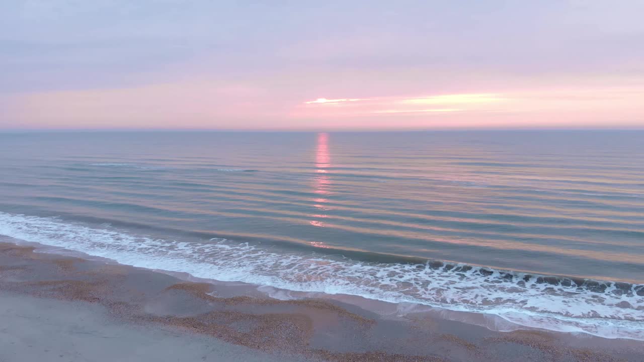 海上日落。美丽的粉红色日出与巨大的波浪。日落时分，海浪拍打着沙滩，溅起白色的泡沫视频素材