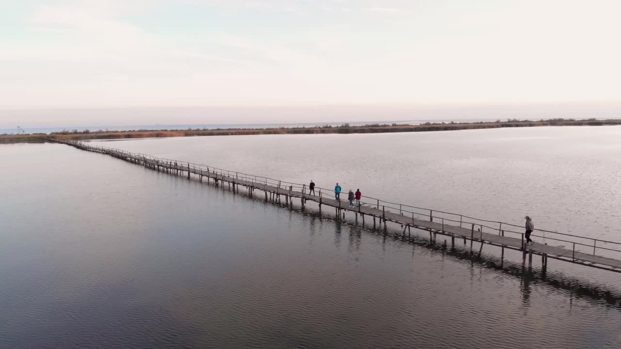 人们走在木桥上，穿过水面平静的河口。平静的湖在秋天的风景。野生自然视频素材