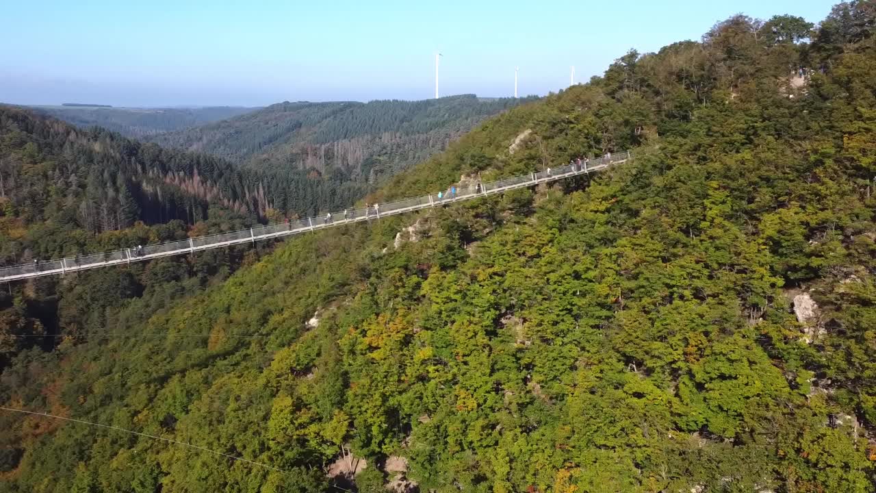 一架无人机飞过一座悬挂着钢索的木桥，俯瞰着西德一片茂密的森林，可以看到游客在桥上行走。视频素材