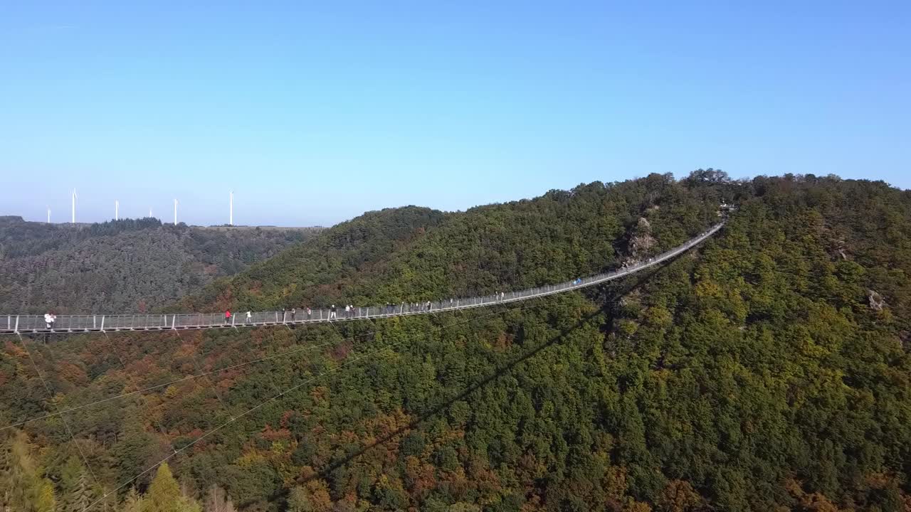 一架无人机飞过一座悬挂着钢索的木桥，俯瞰着西德一片茂密的森林，可以看到游客在桥上行走。视频素材