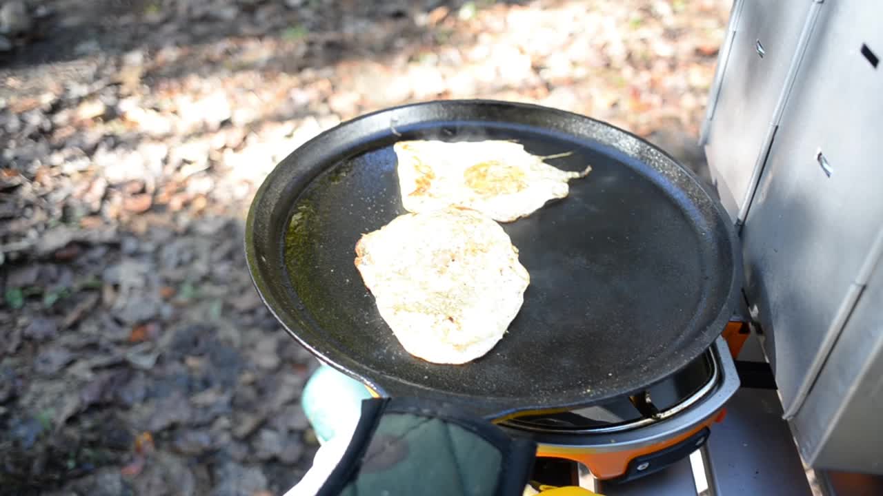 在野营炉铸铁煎锅上煎鸡蛋，烤箱附近煎熟香肠和饼干视频素材