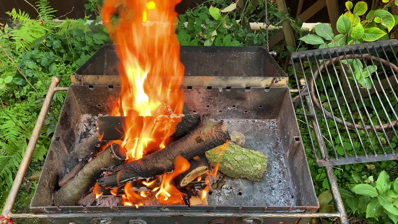 明热的火在干燥的原木和木炭上燃烧，从柴火的户外烧烤架与黄色的舌头火焰和火焰。视频素材