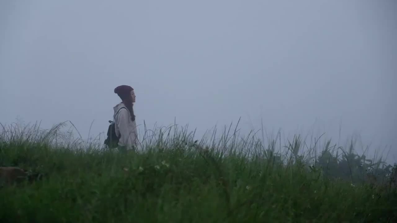 一个女性旅行者在雾天穿过绿色的山脉的慢镜头视频素材