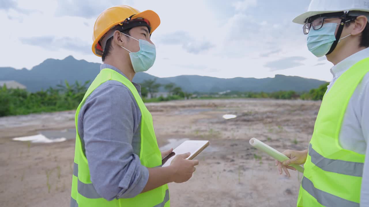 两名年轻的工程人员戴着防护口罩，计划在室外泥土施工现场工作，在新冠疫情期间自我预防，聘请专业施工团队视频素材