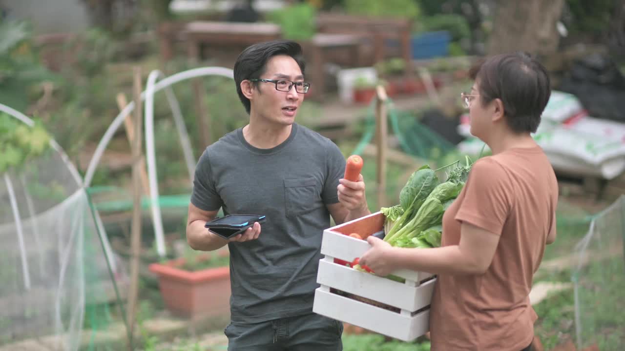 可持续的生活方式亚洲华人中年男子在后院的菜园向他的伴侣展示收获的本地农产品视频素材