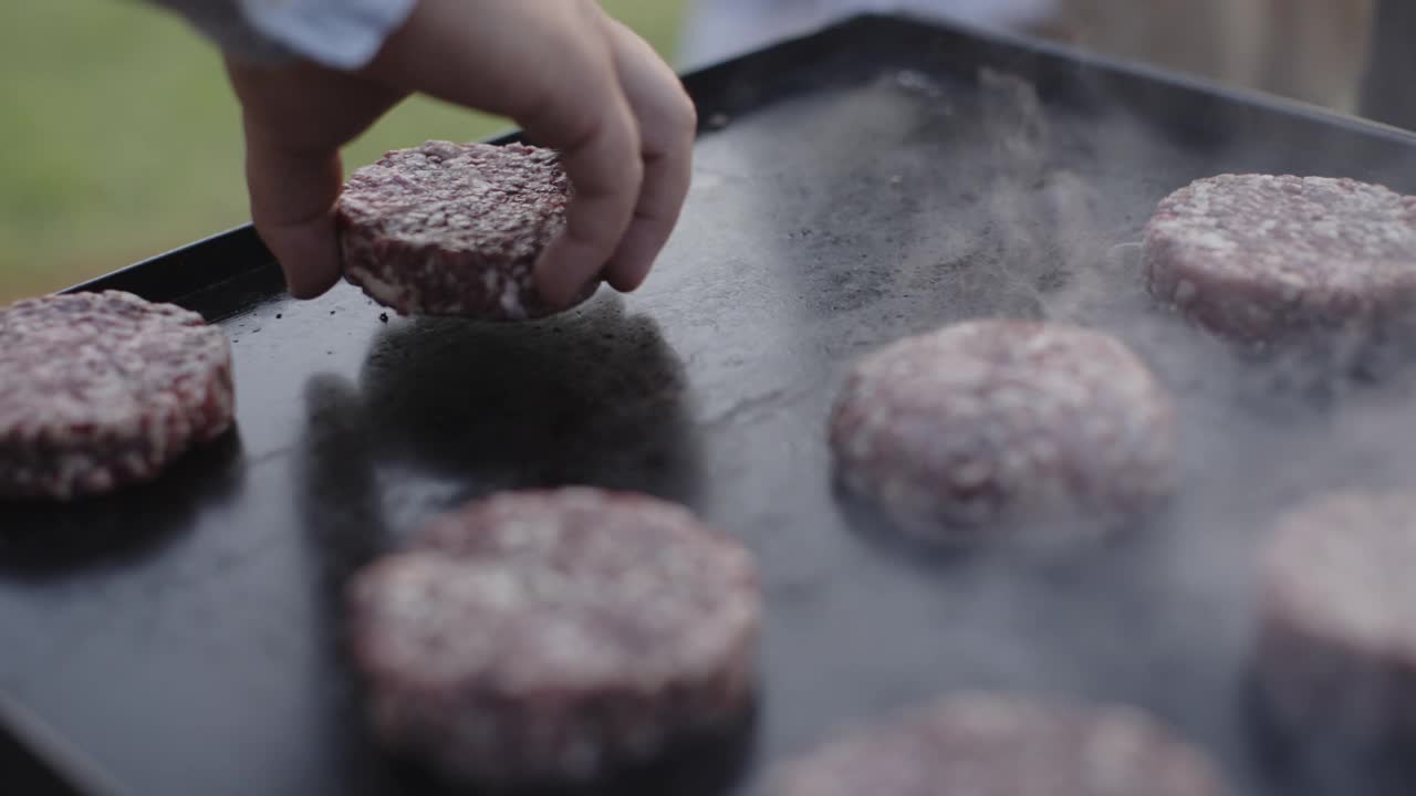 近距离的手放置牛肉汉堡在一个石头板上的木材烧烤视频素材