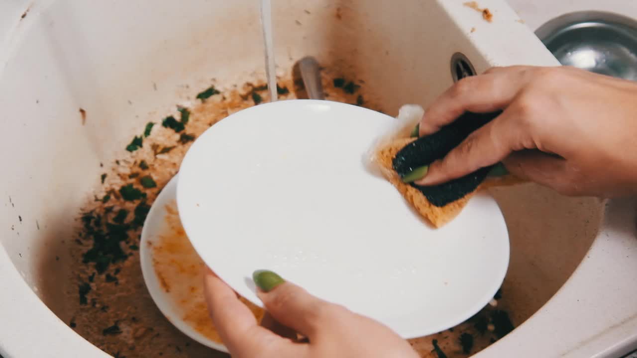 年轻女子在厨房的脏水槽里洗盘子，慢动作视频素材