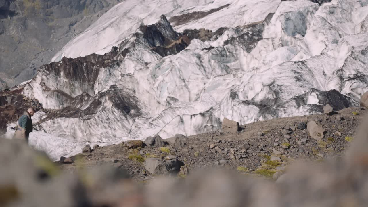 旅行者携带吉他盒在岩石山旁边的冰川视频素材