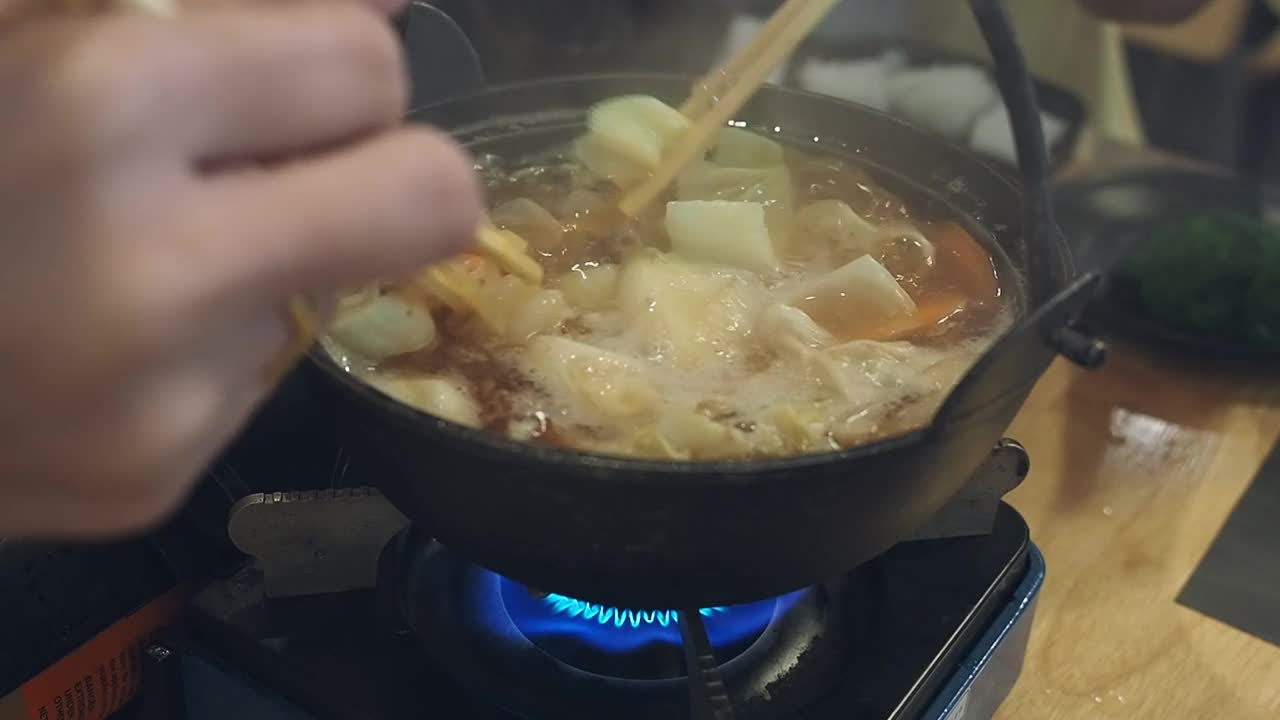 在一家日本餐馆里，餐桌上的每个人都用筷子从涮锅里抓取食物(猪肉、牛肉、蔬菜、海鲜)。视频素材