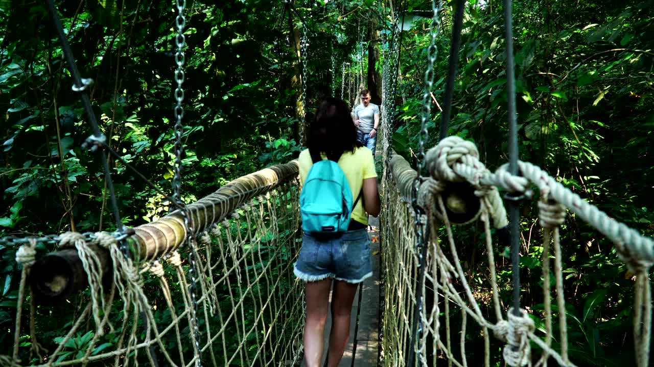 一对年轻的白种人夫妇在悬崖上热带森林的吊桥上徒步旅行视频素材