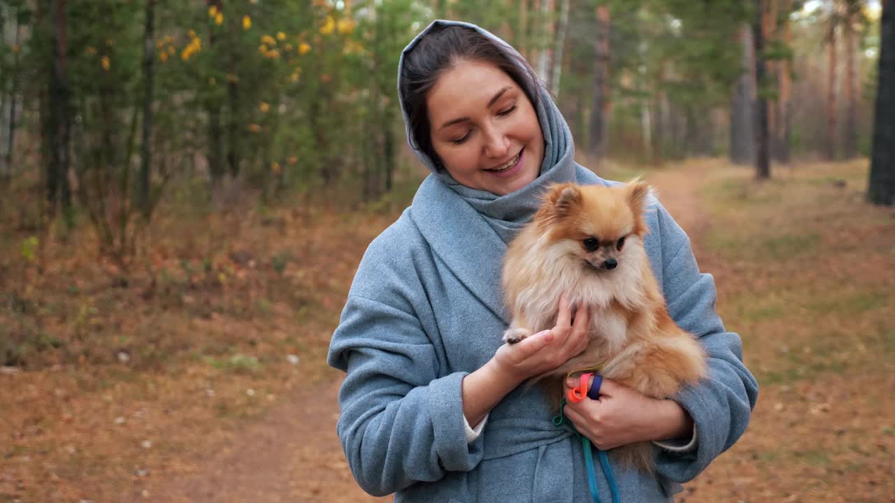 一名年轻女子抱着波美拉尼亚迷你斯皮兹在秋天公园散步视频素材