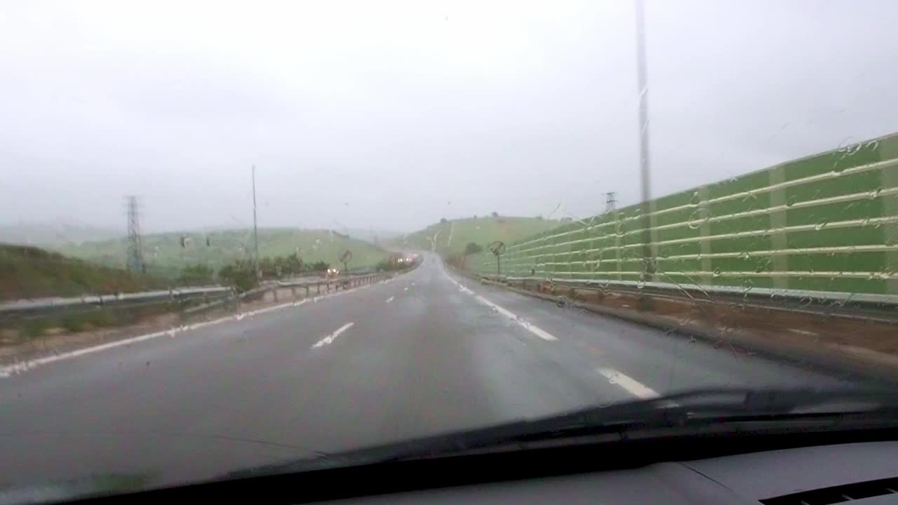 在大雨中行驶时，透过车窗看到的道路。雨中汽车挡风玻璃上的交通景象。视频下载