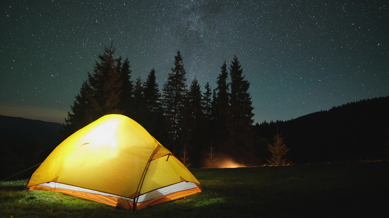 夜晚的星空下，明亮的帐篷在黑暗的山上闪闪发光。积极的生活方式和徒步旅行的理念视频素材