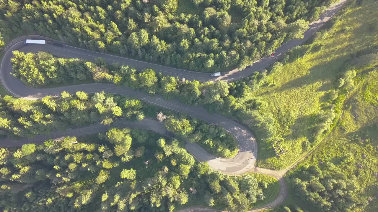 鸟瞰图的蜿蜒的道路与割草汽车和卡车在高山口，槽茂密的树林。视频素材