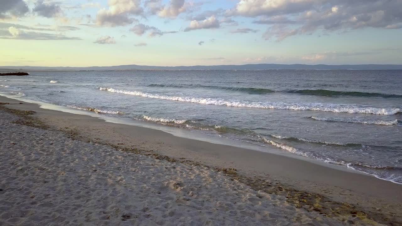 鸟瞰图的海面与蓝色的波浪在紫色的日落天空下。视频素材